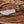 D2 steel tracker knife with Micarta handle, blade tip pointing left, notched spine, and paracord on wood background