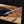 Hand holding a knife with a black and blue handle over a wooden surface.