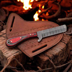 A fixed-blade knife with a patterned steel blade and a red-and-black wood handle rests on a brown leather sheath placed on a rustic log with visible flames in the background.