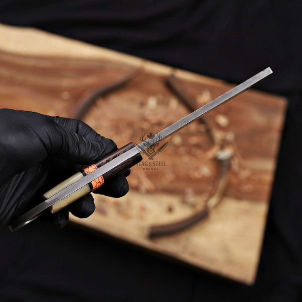 Hand holding a knife with 'Hag & Steel Knives' branding on a wooden background
