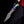 A close-up of a custom San Mai Damascus Bowie knife with a patterned San Mai Damascus steel blade and a colorful resin handle, held by a person wearing a black glove and black pants against a solid black background.