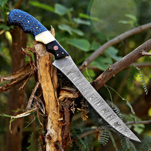 A fixed-blade knife with a patterned steel blade and a blue honeycomb-textured handle, shown resting on a tree branch in an outdoor forest setting.
