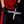 A close-up of a person wearing black gloves and a red shirt, holding a large Finger Guard Bowie knife with a San Mai Damascus steel blade and resin handle cutting the firewood.