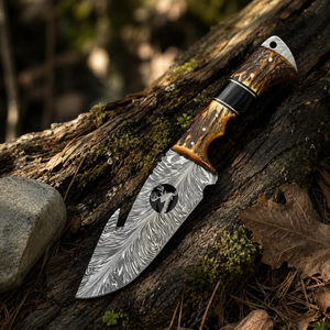 A custom fixed-blade knife with a patterned steel blade and a multi-material handle, resting on a mossy log in an outdoor forest setting.