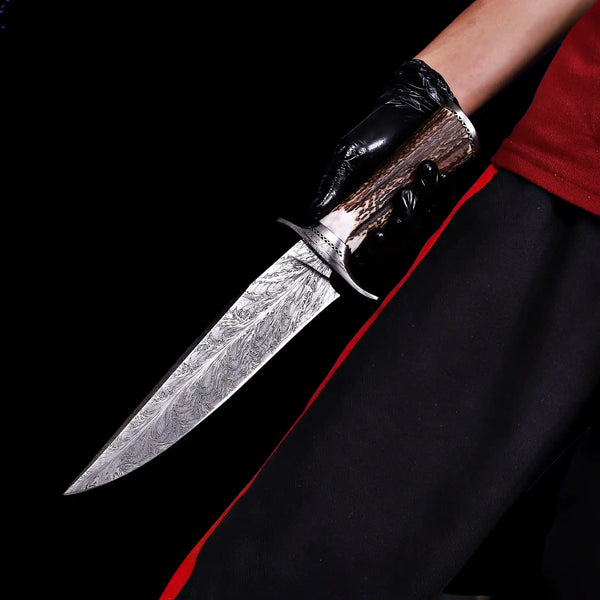 Feather Damascus bowie knife with antler handle held against black background