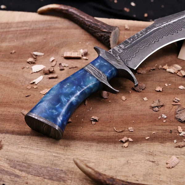 Rear view of Damascus finger guard bowie knife with blue resin handle on wooden board