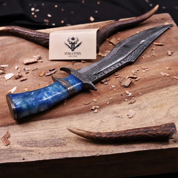 Finger guard Damascus bowie knife displayed on rustic workbench with antlers