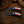 Two curved folding knives with Texas flag-patterned handles are displayed on a rustic wooden surface alongside a brown hat and rope.
