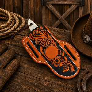 A handcrafted orange and black leather knife sheath with western-style tooling, displayed on a rustic wooden surface alongside a rope, leather gloves, and a cowboy hat.