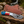 A custom fixed-blade gut hook knife with a patterned steel blade, a blue and red handle, and a brown leather sheath, displayed on a rustic log with a blurred outdoor background.