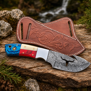 A custom fixed-blade gut hook knife with a patterned steel blade, a blue and red handle, and a brown leather sheath, displayed on a rustic log with a blurred outdoor background.
