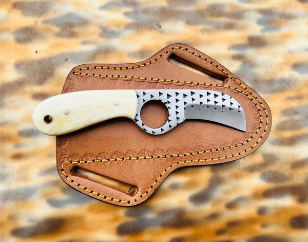 A fixed-blade knife with a patterned silver blade and cream-colored handle, resting on a brown leather sheath over a leopard-print background.