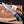 A hand wearing a black glove holds a fixed-blade knife with a patterned steel blade and a colorful handle. The knife is positioned over a wooden cutting board with wood shavings, antlers, and a small branded card in the background.