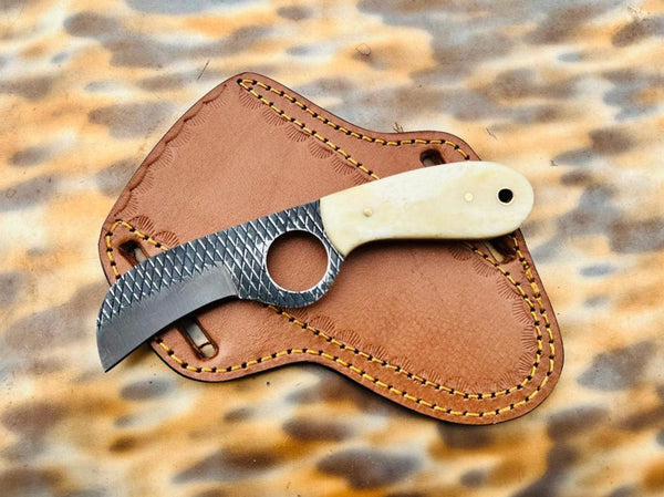 A fixed-blade knife with a textured dark gray blade and a cream-colored handle, resting on a brown leather sheath over a leopard-print fabric background.