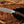 Knife with a wooden handle held by a gloved hand on a wooden surface with dried leaves.