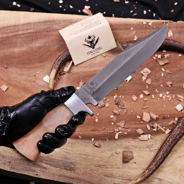 Gloved hand gripping lacewood handle of full tang D2 hunting knife over board