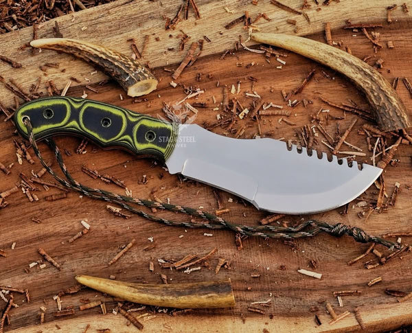 Handmade D2 tracker knife with green Micarta handle, mirror polished blade, paracord, and antler accents on rustic wood