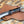 Custom handmade rasp steel hawkbill knife with a black, orange, and white swirled resin handle and ring pommel, resting on a light brown basket-weave leather sheath.
