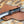 A hawkbill knife with a black and copper marbled handle and a partially serrated blade, resting on a brown woven leather sheath over a leopard-print background.