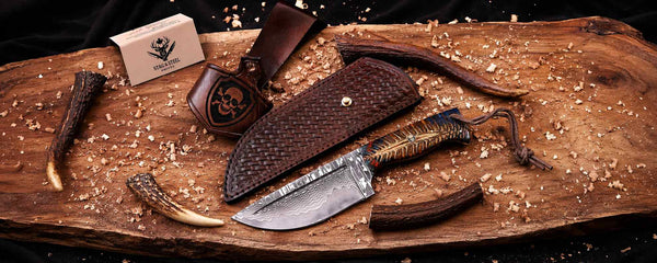 Handmade damascus hunting knife and sheaths on a wooden surface with visible brand logo.
