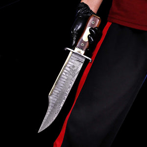 Iron Mistress Damascus bowie knife with brass spine held against black background