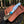 A fixed-blade knife with a patterned silver blade, a turquoise inlay, and a bone handle rests on a brown embossed leather sheath outdoors on a log, with a forest background.