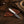 A small fixed-blade knife with a patterned steel blade and white handle rests on a brown leather sheath, placed on a rustic wooden surface with a cowboy hat, rope, and wood props nearby.