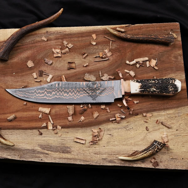 copper damascus bowie knife with antler handle laying wooden backround