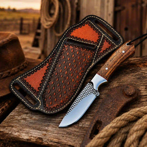 A handcrafted knife with a patterned wooden handle and textured steel blade, displayed next to its matching brown leather sheath on a rustic wooden surface.