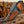 A custom knife with a patterned steel blade and a hand-tooled brown handle, displayed in a matching brown leather sheath with blue and brown floral inlay, set on a rustic wooden log with a blurred western background.