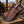 A hand-tooled leather sheath with intricate geometric patterns and white stitching, featuring a decorative handle with blue accents, resting on a rustic wooden surface with a blurred western background.
