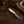 A small fixed-blade knife with a patterned steel blade and a white handle with a blue accent line, resting on a rustic dark wood surface. A brown cowboy hat, leather strap, wood pieces, and rope are styled around it.