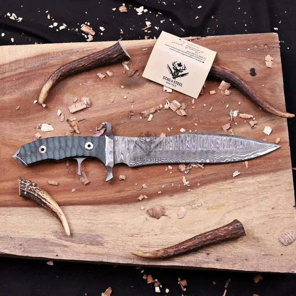 Full view of custom Damascus bowie knife with double finger guard staged on wooden board with antler horn accents
