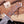 A close-up of a custom fixed-blade knife with a textured brown wooden handle and a silver steel blade, resting on a rustic wooden surface with blurred wood pieces in the background.