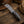 A custom knife with a patterned gray steel blade and a blue marbled handle, displayed diagonally on a rustic wooden surface next to a brown leather hat and a coil of rope.