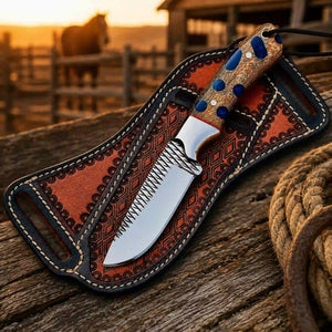 A fixed-blade knife with a textured silver blade and a carved handle lies inside a decorative brown leather sheath on a rustic wooden surface. The background shows a blurred outdoor ranch scene at sunset with a horse and fence.